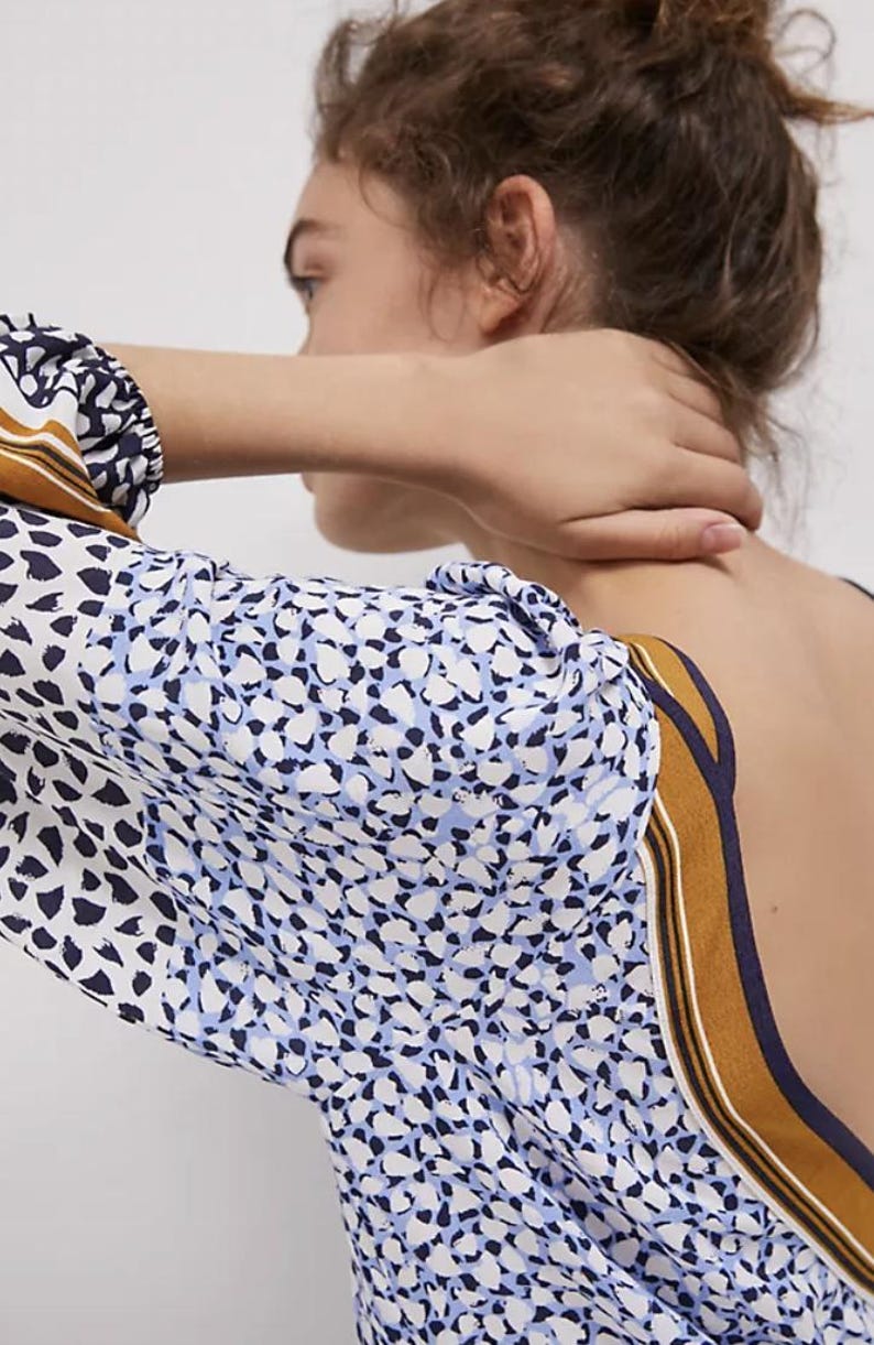 Puede incluir: Top estampado con mangas largas. La tela presenta un dise&ntilde;o de formas blancas, azul marino y celeste. El escote y los pu&ntilde;os de las mangas tienen un detalle de rayas marrones y azul marino. La espalda del top est&aacute; abierta.