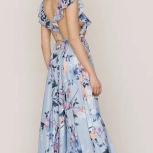 May include: A light blue floral print maxi dress with a flowing skirt and open back. The dress features a ruffled neckline and straps, with a pattern of blue, pink, and purple flowers.