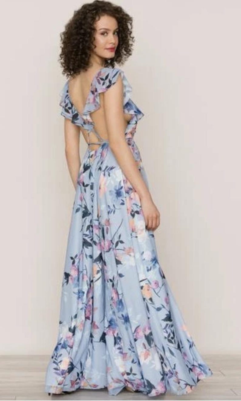May include: A light blue floral print maxi dress with a flowing skirt and open back. The dress features a ruffled neckline and straps, with a pattern of blue, pink, and purple flowers.