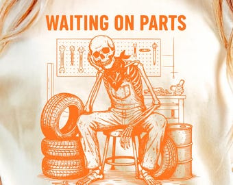 May include: Cream-colored t-shirt with an orange graphic of a skeleton in overalls, leaning on a hand, with the text "WAITING ON PARTS". The skeleton is in a garage setting with tires, tools, and barrels.