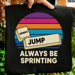 May include: Black tote bag with a retro sunset design. The design features keyboard keys with the words "SPRINT" and "JUMP", and the phrase "ALWAYS BE SPRINTING" in white. The background has horizontal stripes of purple, orange, and blue.