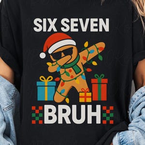 May include: Black t-shirt with a Christmas-themed graphic. The design features a gingerbread man wearing sunglasses and a Santa hat, with the words "SIX SEVEN BRUH" in white. Colorful gift boxes and Christmas lights are also included.