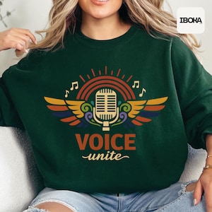 May include: A dark green sweatshirt with a colorful graphic featuring a microphone, rainbow, musical notes, and wings. The words "VOICE unite" are printed below the microphone in orange and white.