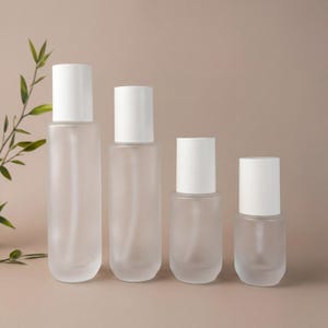 Könnte beinhalten: Vier Flaschen aus mattiertem Glas mit weißen Kappen in verschiedenen Größen sind in einer Reihe angeordnet. Die Flaschen sind zylindrisch und oval geformt, mit einem minimalistischen Design. Der Hintergrund ist in einem neutralen Beige gehalten.