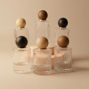 Puede incluir: Botellas de vidrio transparente con lados acanalados y tapones esféricos de madera. Los tapones son de varios tonos de marrón y beige. Las botellas están dispuestas sobre un fondo neutro.