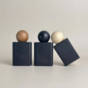 May include: Three abstract wooden sculptures. Each sculpture features a black rectangular base topped with a wooden sphere. The spheres are natural wood, black, and light wood. One base is tilted.