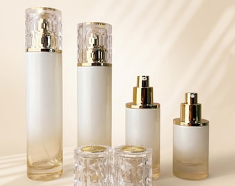 May include: Four cylindrical cosmetic bottles with a white to clear gradient finish and gold pump dispensers. Two taller bottles feature faceted, clear, diamond-like caps, while two shorter bottles have exposed gold pump heads and separate caps.