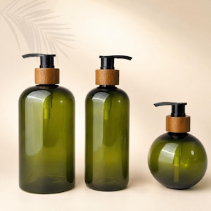May include: Three dark green translucent soap dispensers with black pump mechanisms and light brown wooden collars. Two bottles are tall and cylindrical, while the third bottle is spherical in shape. Each dispenser features a clear plastic tube inside.
