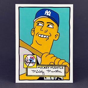 May include: A baseball card featuring a cartoon depiction of Mickey Mantle in a New York Yankees uniform. The card has a blue background and a yellow border with the text "Mickey Mantle". The Yankees logo is also visible.