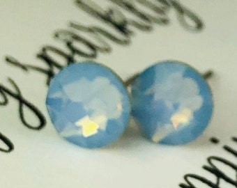 May include: A pair of small, round, light blue earrings with a white iridescent shimmer. The earrings are stud style.