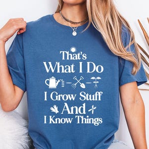 May include: Indigo blue t-shirt with the text "That's What I Do, I Grow Stuff And I Know Things" in white. The design includes gardening tools and a watering can. The shirt is a crew neck and has short sleeves.