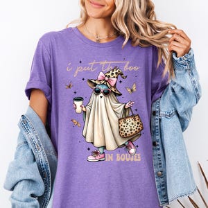 May include: A heather purple t-shirt featuring a graphic of a ghost wearing a leopard print witch hat, pink sunglasses, and pink sneakers. The ghost holds a coffee cup and a leopard print handbag. The text reads, I put the boo in boujee.