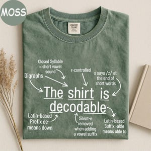 May include: A moss green t-shirt with white text that reads The shirt is decodable, surrounded by linguistic annotations including Digraphs, Closed Syllable, r-controlled, s says /z/, Latin-based Prefix de-, Silent-e, and Latin-based Suffix -able.