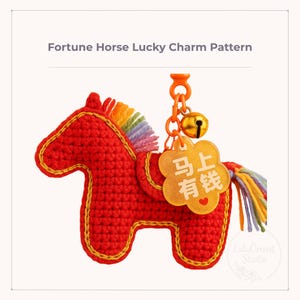 Può includere: Un ciondolo a forma di cavallo rosso all'uncinetto con finiture dorate, criniera e coda arcobaleno e una campana dorata. Il ciondolo ha un'etichetta dorata con caratteri cinesi. Il testo "Fortune Horse Lucky Charm Pattern" è in alto.