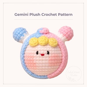May include: A handmade Gemini plush crochet pattern in pastel colors. The plushie features a round head with blue and pink sections, small yellow accents, and a smiling face. The text "Gemini Plush Crochet Pattern" is at the top.