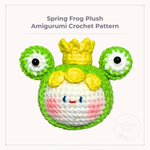 May include: A handmade amigurumi crochet frog plush toy. The frog is primarily green and white, with a yellow crown and accents. The frog has large, round eyes and rosy cheeks. Text on the image reads "Spring Frog Plush Amigurumi Crochet Pattern."