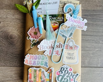 May include: A brown paper envelope filled with stationery items including a reading list card, a light blue tassel, two blue pens, a butterfly paperclip, and various stickers featuring text like Mood Reader, Booktrovert, and Good Day to Read.