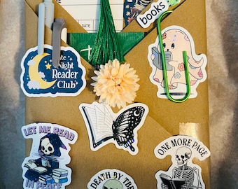 May include: A wrapped package with stickers and a green tassel. Stickers include a skeleton reading, a butterfly, and the text "READING LIST". The package is decorated with a light orange flower and a green paper clip.