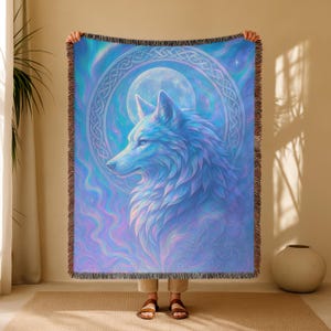 Peut inclure: Une couverture tissée avec une illustration détaillée d'un loup et d'une pleine lune. Le loup est représenté dans des tons de bleu et de violet, avec un motif de nœud celtique autour de la lune. La couverture a une bordure frangée.