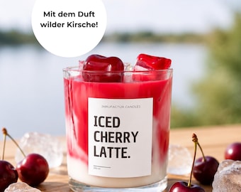 Könnte beinhalten: Eine Glaskerze mit einem weißen Etikett mit der Aufschrift "JANUFACTUR CANDLES ICED CHERRY LATTE. 200 ml" und einer weißen Sprechblase mit dem Text "Mit dem Duft wilder Kirsche!". Die Kerze enthält rotes und weißes Wachs mit kirschförmigen Wachsstücken.