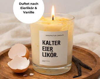 Könnte beinhalten: Eine brennende Kerze in einem durchsichtigen Glas mit einem Etikett mit der Aufschrift "KALTER EIER LIKÖR". Die Kerze steht auf einem Holztablett mit einer Eierschale und Vanilleschoten. Der Text "Duftet nach Eierlikör & Vanille" befindet sich in einem weißen Kreis.