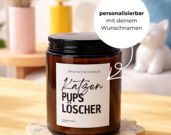 Könnte beinhalten: Ein braunes Glas-Kerzenglas mit schwarzem Deckel und weißem Etikett. Auf dem Etikett steht "Katzen Pups Löscher" in schwarzer Schrift. Die Kerze steht auf einem dekorativen Untersetzer. Der Text "personalizierbar mit deinem Wunschnamen" ist ebenfalls sichtbar.