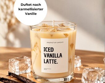 Könnte beinhalten: Eine Kerze in einem klaren Glasbehälter gefüllt mit einer beigen Flüssigkeit, die einem Eiskaffee ähnelt, mit einem weißen Etikett mit der Aufschrift JANUFACTUR CANDLES ICED VANILLA LATTE 200 ml, umgeben von Eiswürfeln und zwei Vanilleschoten.