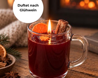 Könnte beinhalten: Ein durchsichtiger Glasbecher gefüllt mit dunkelrotem Wachs, mit brennendem Docht, einer getrockneten Orangenscheibe und einer Zimtstange. Ein weißes, rundes Etikett mit dem schwarzen Text Duftet nach Glühwein befindet sich darüber.