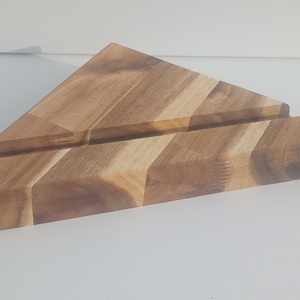 May include: A wooden phone stand with a triangular top and a rectangular base. The stand is made of light and dark brown wood, with visible grain patterns. The stand is designed to hold a phone or tablet.