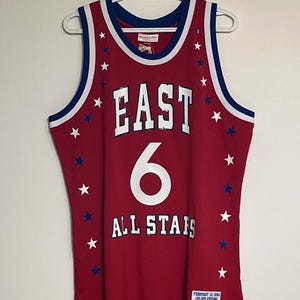 Puede incluir: Camiseta de baloncesto roja con detalles blancos y azules. La camiseta presenta la palabra "EAST" sobre el número "6" y "ALL STARS" en letras blancas. Estrellas blancas y azules salpican la camiseta.