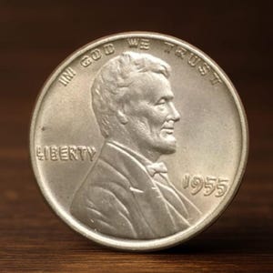 Op de afbeelding: Een zilveren Lincoln-munt uit 1955, met een profiel van Abraham Lincoln. De munt heeft de inscripties "IN GOD WE TRUST" en "LIBERTY". Het jaartal "1955" is zichtbaar op de munt.