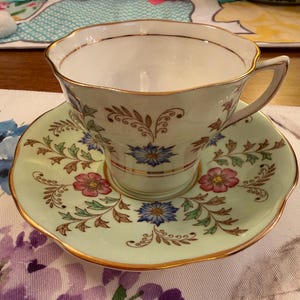 May include: A white ceramic mug with a black handle and the text "But First, Coffee" in a handwritten style. The mug is on a white surface. The mug is approximately 4 inches tall.