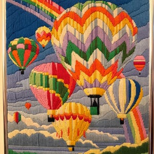 May include: A framed needlepoint artwork featuring colorful hot air balloons against a blue sky with a rainbow. The balloons are various colors, including red, yellow, green, and blue, with detailed stitching.