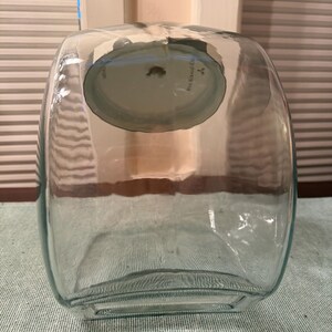 May include: A clear, rectangular glass container with rounded corners and a wide opening at the top. The vessel features a thick, transparent glass construction with a smooth surface and a slightly curved base, designed for storage or display purposes.