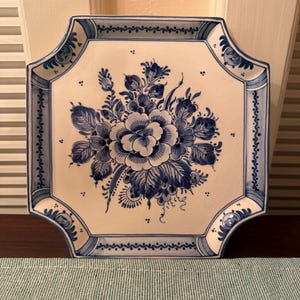 May include: A square ceramic plate with clipped corners, featuring a white base with a blue floral pattern in the center and a blue decorative border. The surface has a visible crackle glaze finish throughout the entire piece.