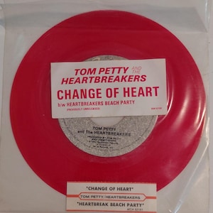 May include: A red vinyl record single by Tom Petty and the Heartbreakers, titled "Change of Heart" and "Heartbreak Beach Party." The record is in a clear plastic sleeve with white labels. The labels include text and the MCA Records logo.