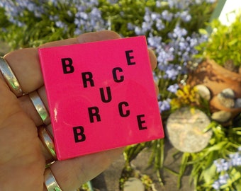 May include: A pink square with the word "BRUCE" spelled out in black letters. The letters are arranged in a diagonal pattern, with the first letter of the word at the top left corner and the last letter at the bottom right corner.