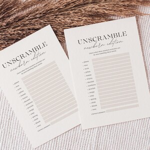 Könnte beinhalten: Zwei cremefarbene Unscramble-Spielkarten mit dem Text "UNSCRAMBLE newborn edition". Die Karten haben eine Liste von Wörtern zum Entwirren. Der Hintergrund ist eine neutrale Farbe mit getrockneten Pflanzen.