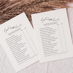 Könnte beinhalten: Zwei cremefarbene Karten mit dem Text "higher or lower" in eleganter Schrift. Die Karten enthalten eine Liste von Fragen mit Antwortmöglichkeiten. Getrocknete Weizenhalme sind im Hintergrund. Ein Babyparty-Spiel.