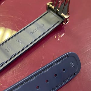 May include: A close-up of a navy blue watch strap with black stitching and a metal clasp. The strap has the number "20" printed on it, along with the text "GJD" and "CV200179".