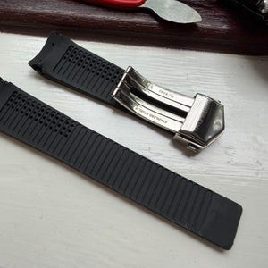 May include: A black rubber watch strap featuring a textured surface with small perforations near the lug end. The strap includes a silver-toned stainless steel deployment clasp with the text "STAINLESS STEEL" and "FC 5030" engraved on the metal.