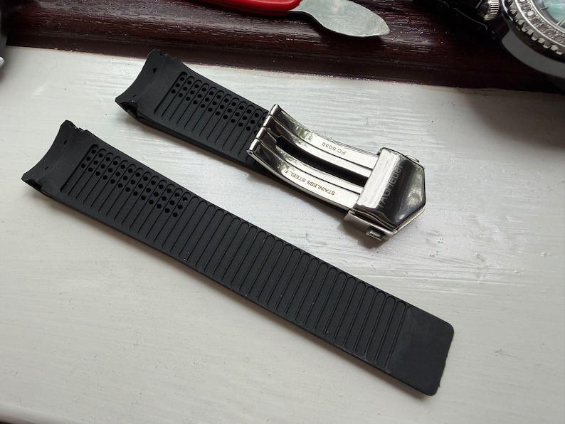 May include: A black rubber watch strap featuring a textured surface with small perforations near the lug end. The strap includes a silver-toned stainless steel deployment clasp with the text "STAINLESS STEEL" and "FC 5030" engraved on the metal.