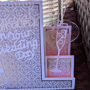 May include: A layered greeting card featuring a white and gold damask pattern, a die-cut champagne flute, and a heart shape. The card displays the text "Beautiful on your Wedding Day" and is decorated with small white pearls along the bottom edge.