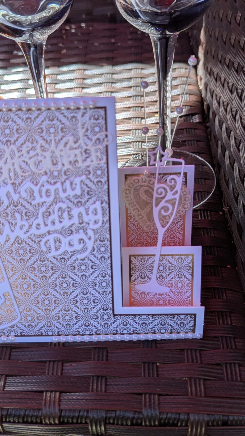 May include: A layered greeting card featuring a white and gold damask pattern, a die-cut champagne flute, and a heart shape. The card displays the text "Beautiful on your Wedding Day" and is decorated with small white pearls along the bottom edge.