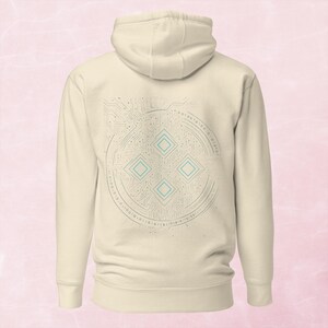 May include: Cream-colored hoodie with a circuit board design on the back. The design includes a circular pattern with binary code and four light blue diamond shapes. The hoodie has a hood and long sleeves.
