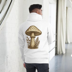 May include: White hoodie featuring a large mushroom graphic on the back. The mushroom is brown with a dotted cap, and is surrounded by botanical illustrations. The hoodie has a drawstring hood and long sleeves.