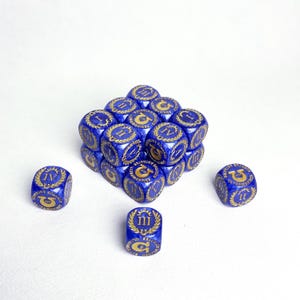 May include: A collection of blue dice with gold markings, arranged in a cube shape. Each die features Roman numerals and decorative emblems. The dice are set against a white background, highlighting their detailed design.