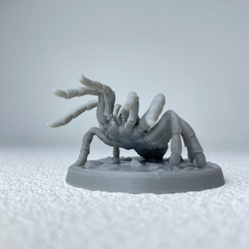 May include: A gray, 3D-printed miniature of a tarantula spider. The spider has multiple legs, a segmented body, and is posed on a circular base. The miniature is detailed and suitable for tabletop gaming or display.