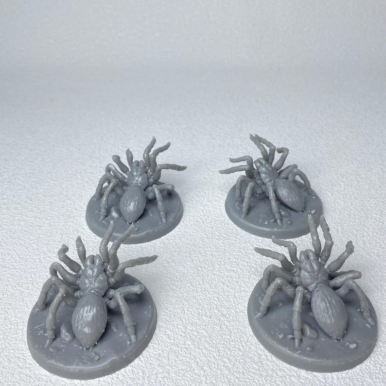 May include: Four gray miniature spider figurines, each with eight legs and a rounded body, are displayed on circular bases. The figurines are designed for tabletop gaming or crafting projects.