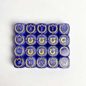 May include: A collection of twenty blue dice with gold Roman numerals and laurel wreaths. Each die features the text "ULTRAMARINES" and "ADEPTUS ASTRATES". The dice are arranged in a grid pattern on a white surface.